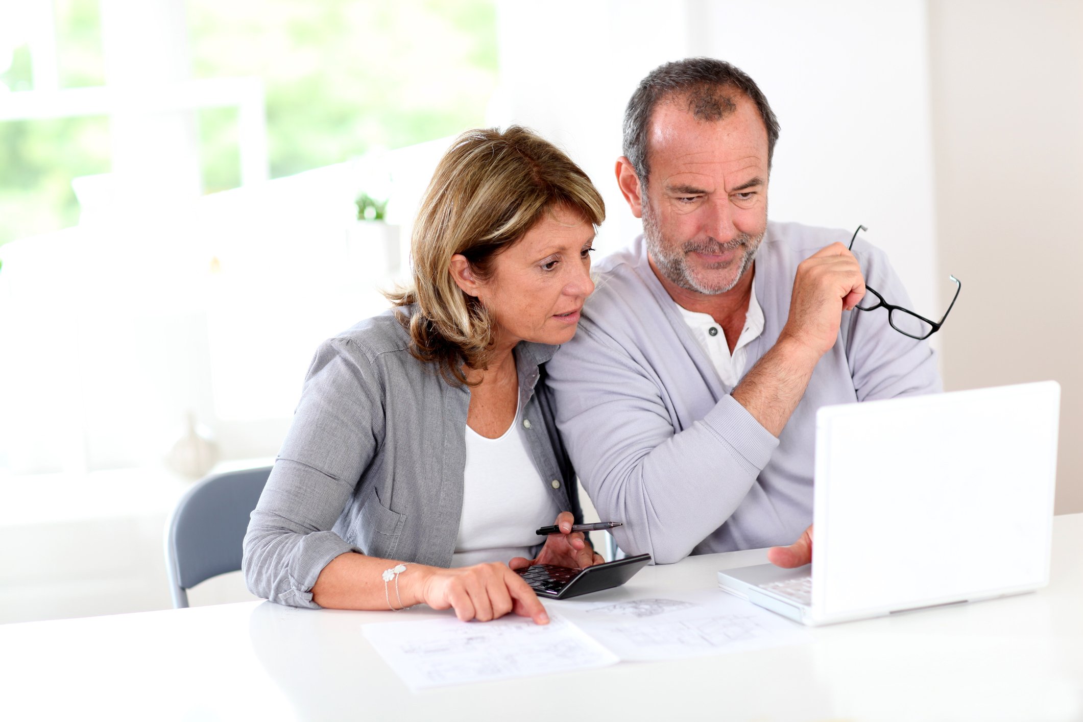 Senior couple looking at laptop on top of a white table. 