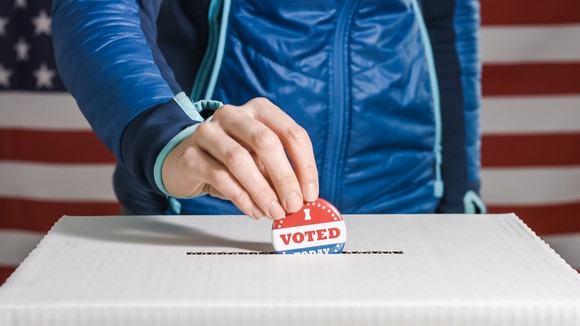 Hand putting I Voted pin into ballot box