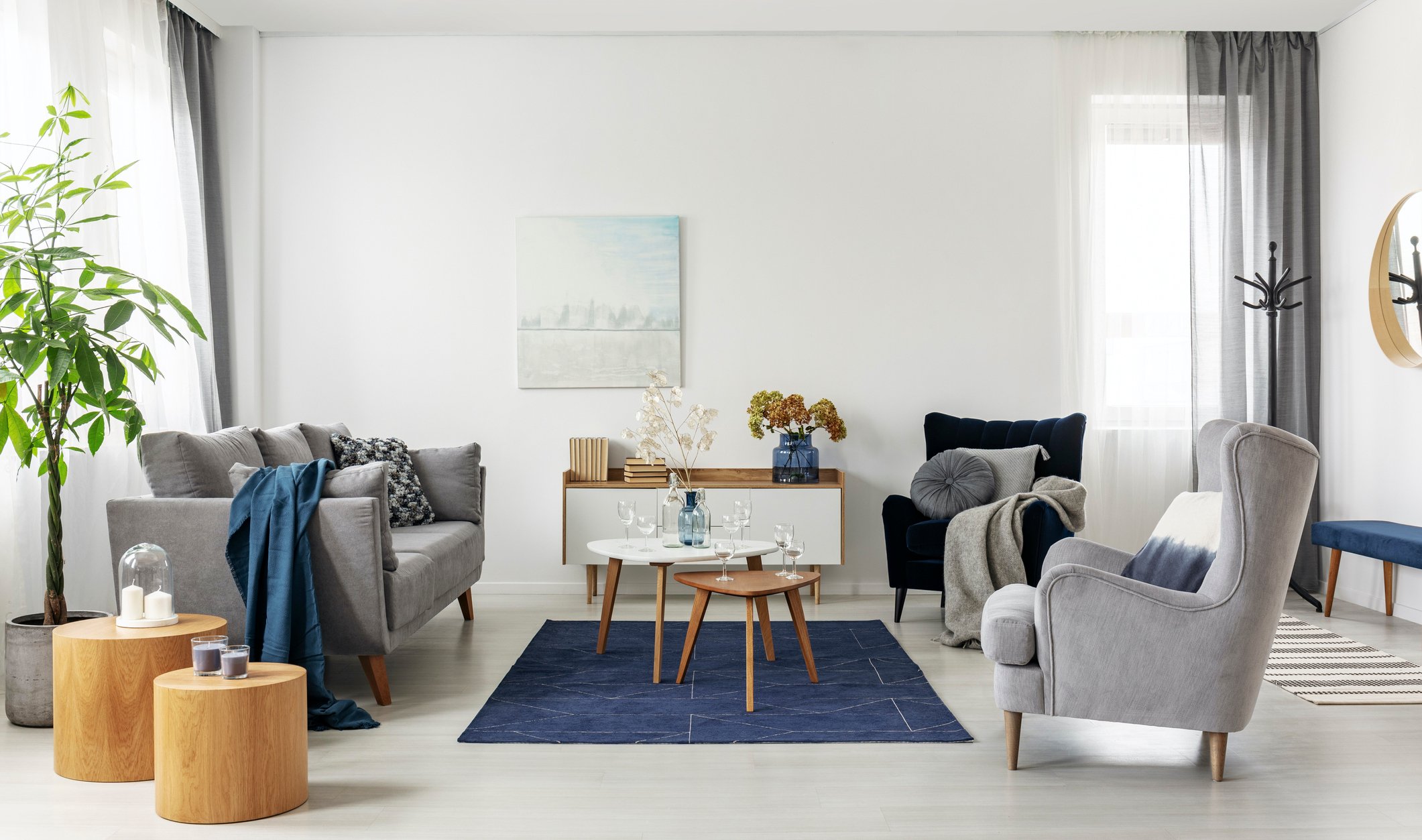 A living room decorated in the mid-century modern style, with two arm chairs, nesting tables, a sofa, and a sideboard