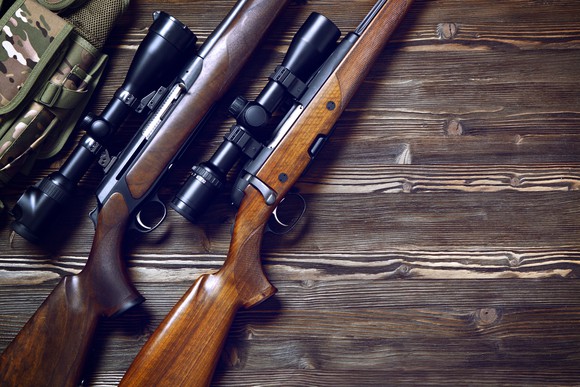 A pair of guns with scopes on a wood table.