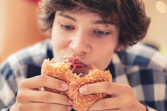 A teenage boy eats a burger.