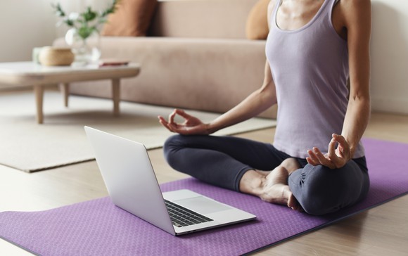 A woman does yoga on a purple yoga mat in front of her computer.