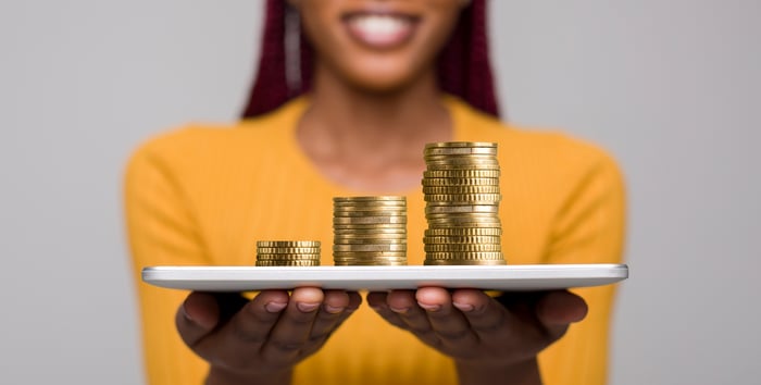 Smiling person holding a tray with three stacks of gold coins rising from left to right. 