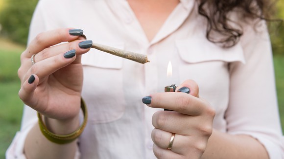 closeup on two female hands one holding a joint and the other lighting it. 