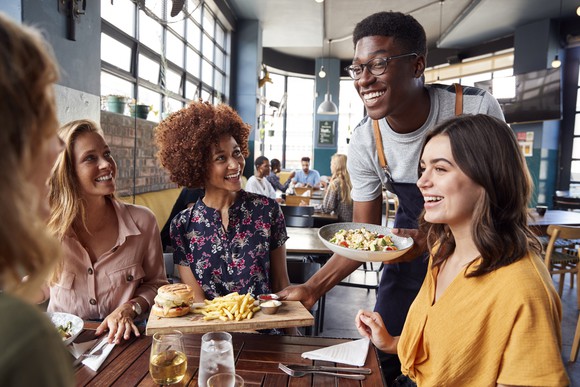 A waiter serves four ladies seating at a table in a casual-dining restaurant.