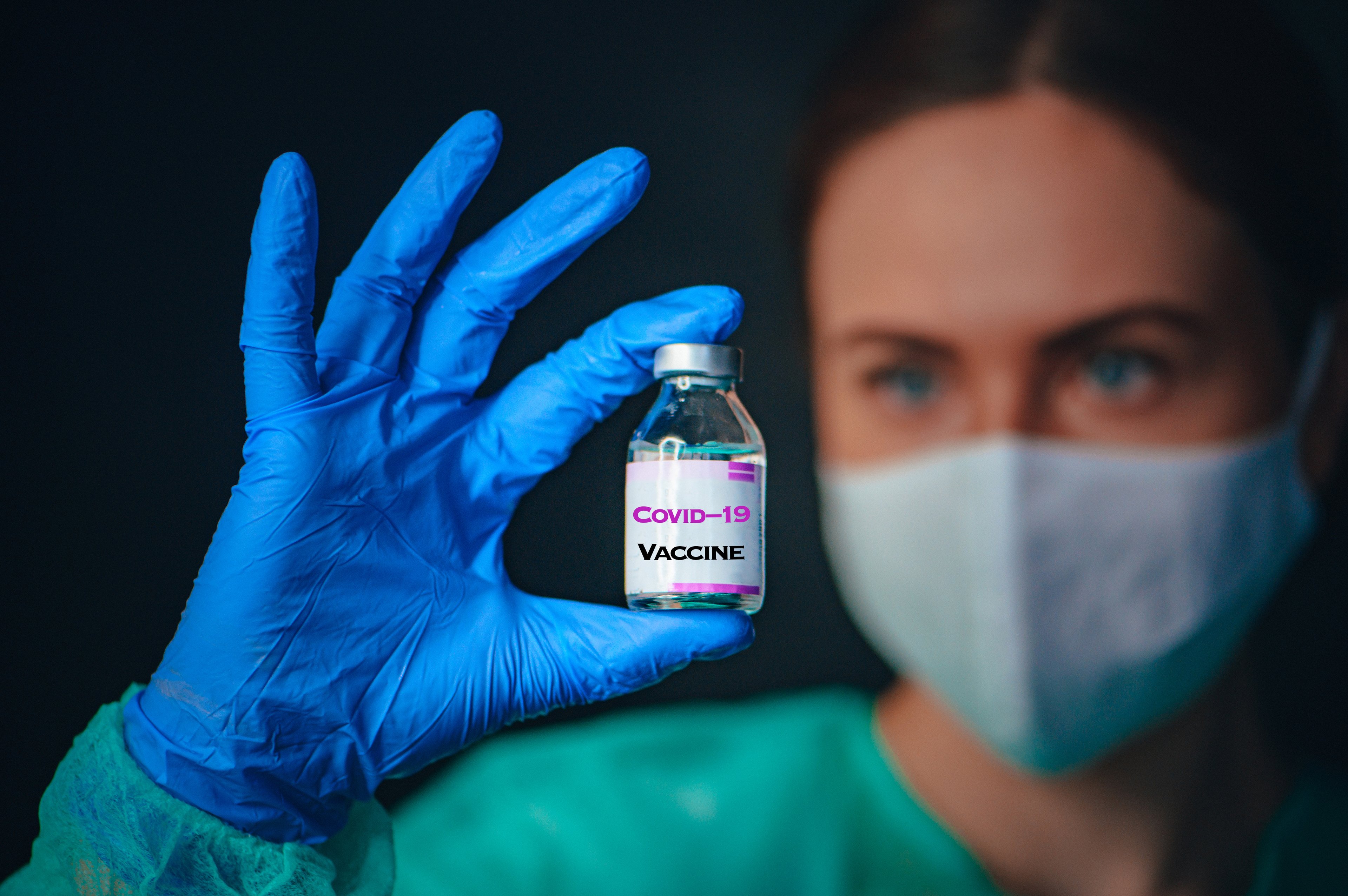 Nurse checking over a  vial labeled COVID-19 vaccine.