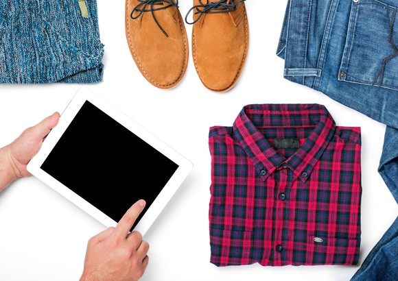 Customer using tablet with a new shirt, jeans, and a pair of shoes laid out on a tabletop.
