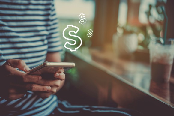 A person on their phone, presumably sending or receiving cash through an app as dollar signs are superimposed coming from the phone. 