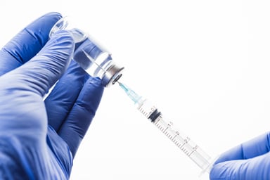 Gloved hands holding vaccine bottle and syringe