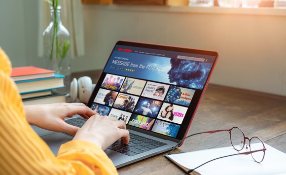 Picture of a person typing on a laptop, watching a streaming video service.