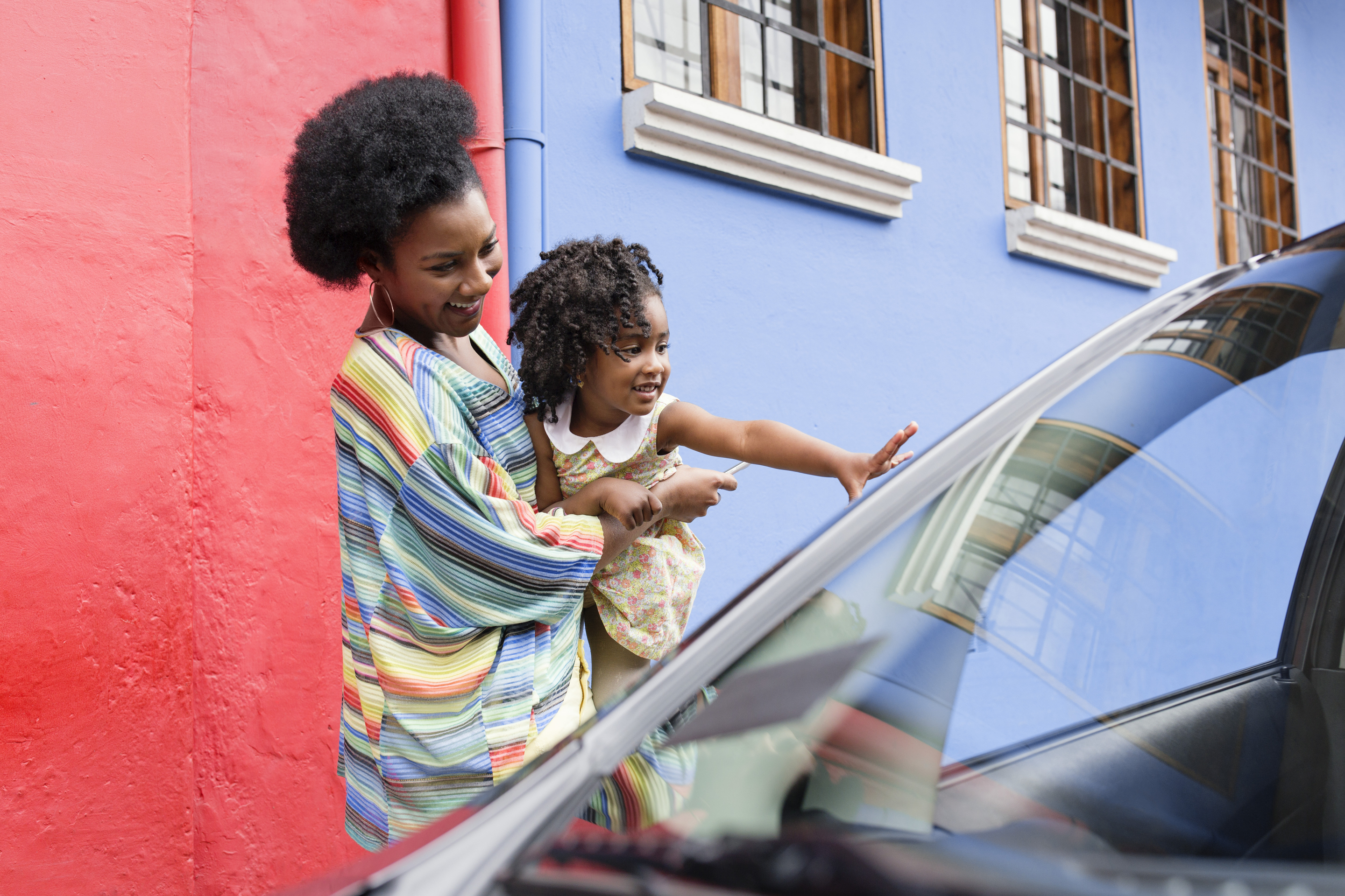 Woman holding child, who's waving to someone in a car.