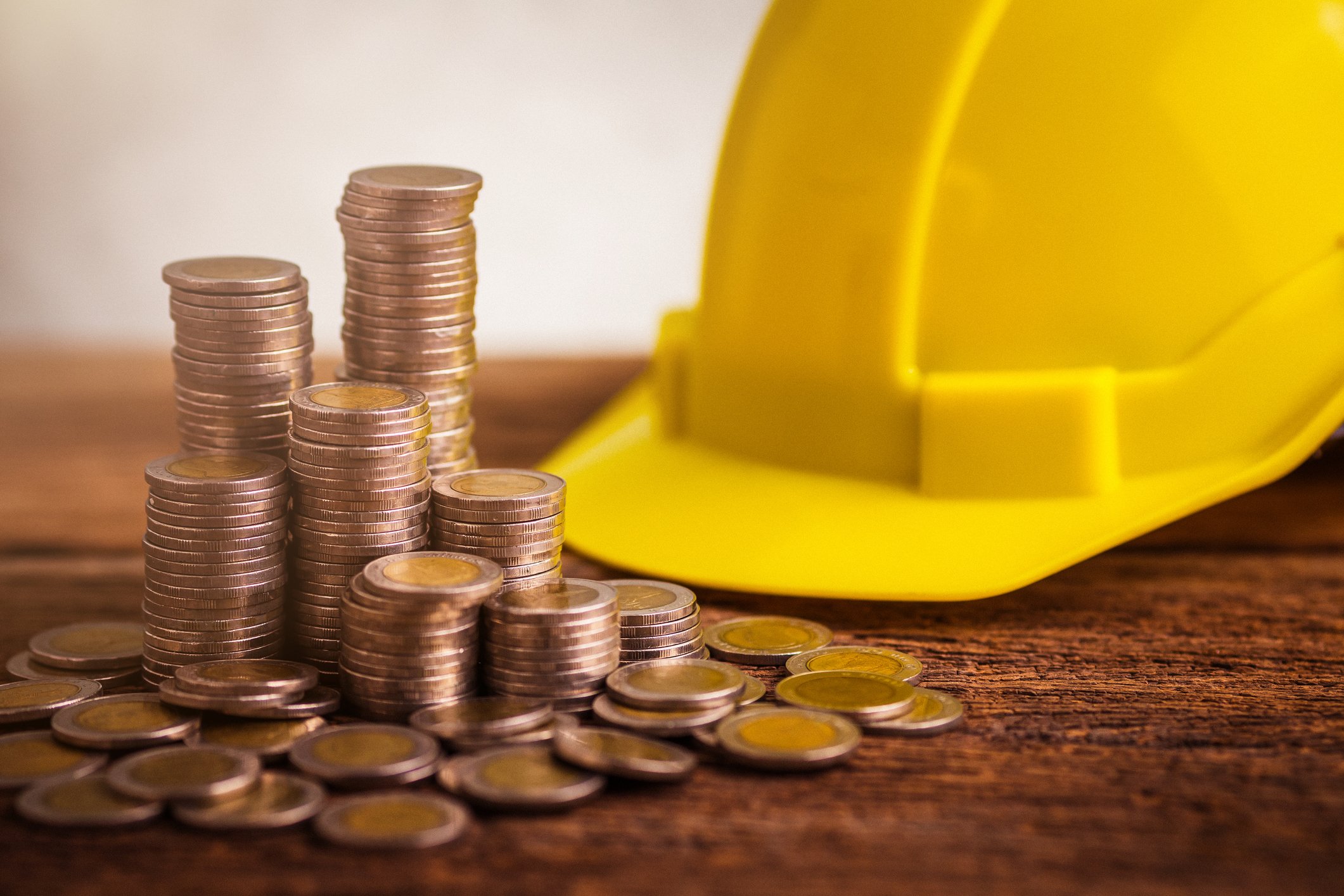 Stacks of coins next to a yellow hard hat on a wooden table