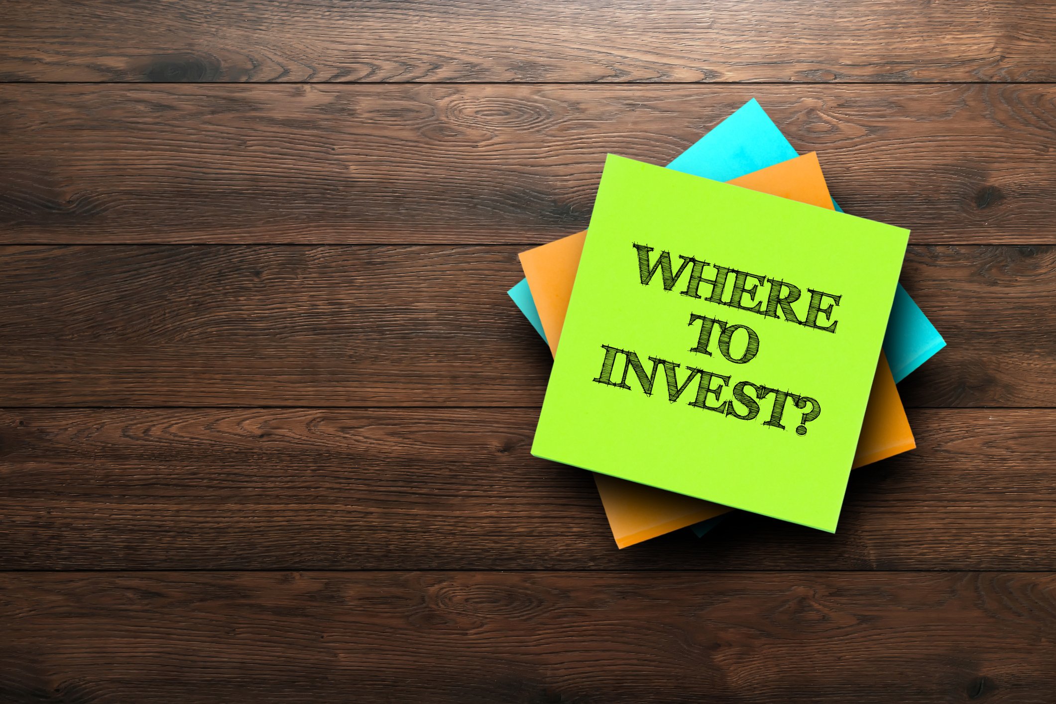 A pile of post-it notes on a table. One asking where to invest? is on top.
