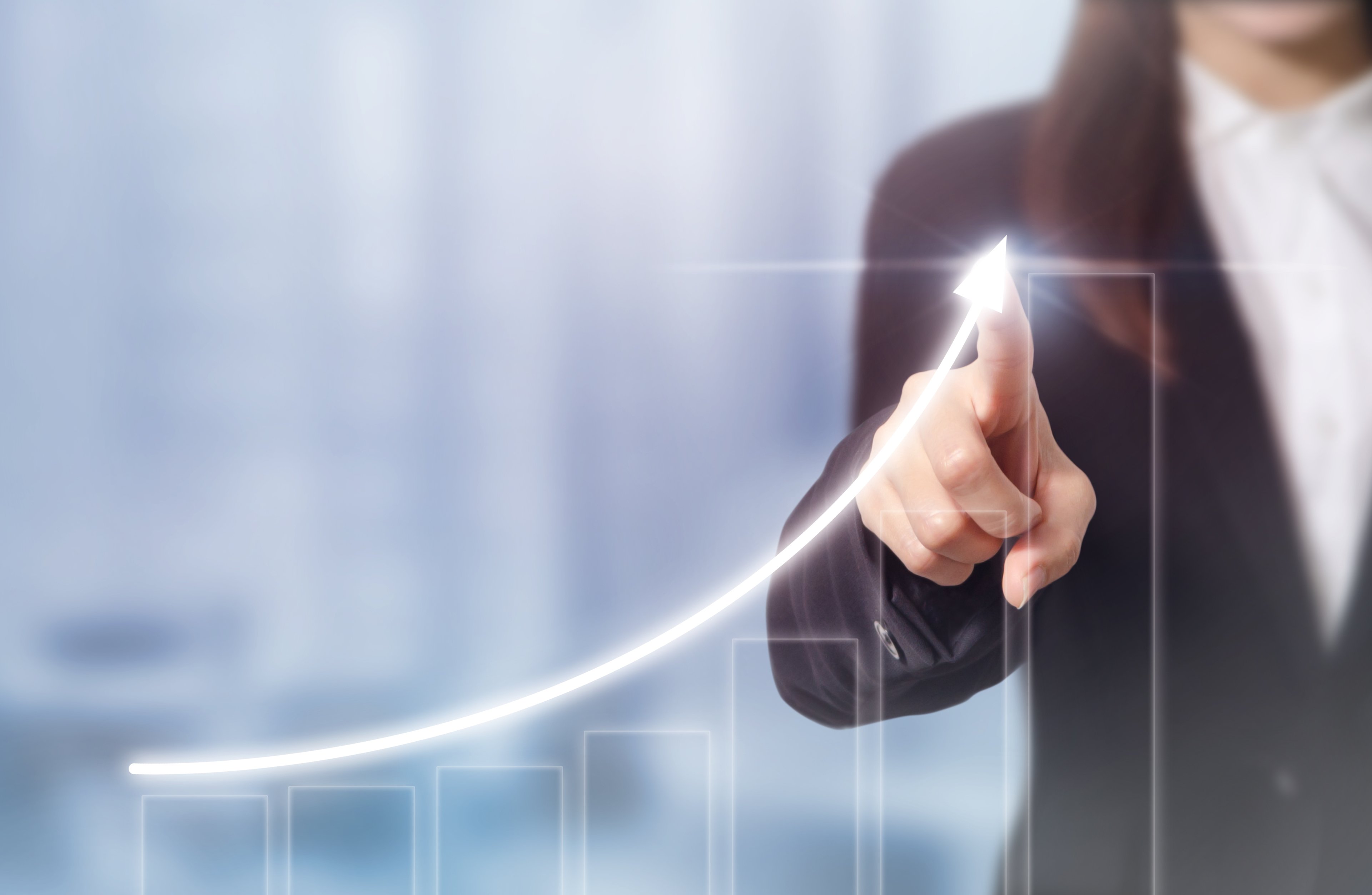 A businesswoman draws an upward arrow on a bar chart displayed on a transparent touchscreen.