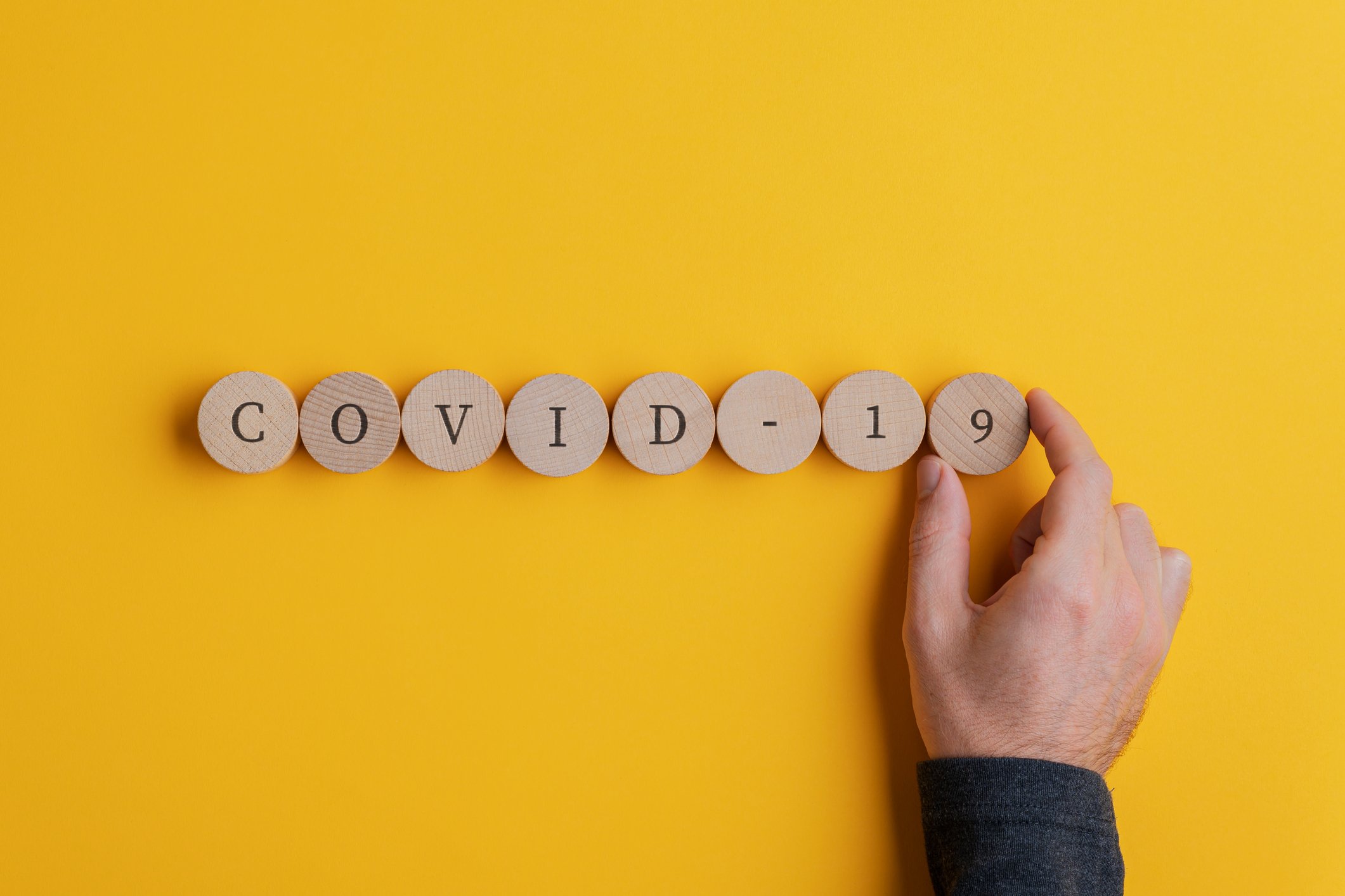 Hand next to COVID-19 spelled out in circular tiles 