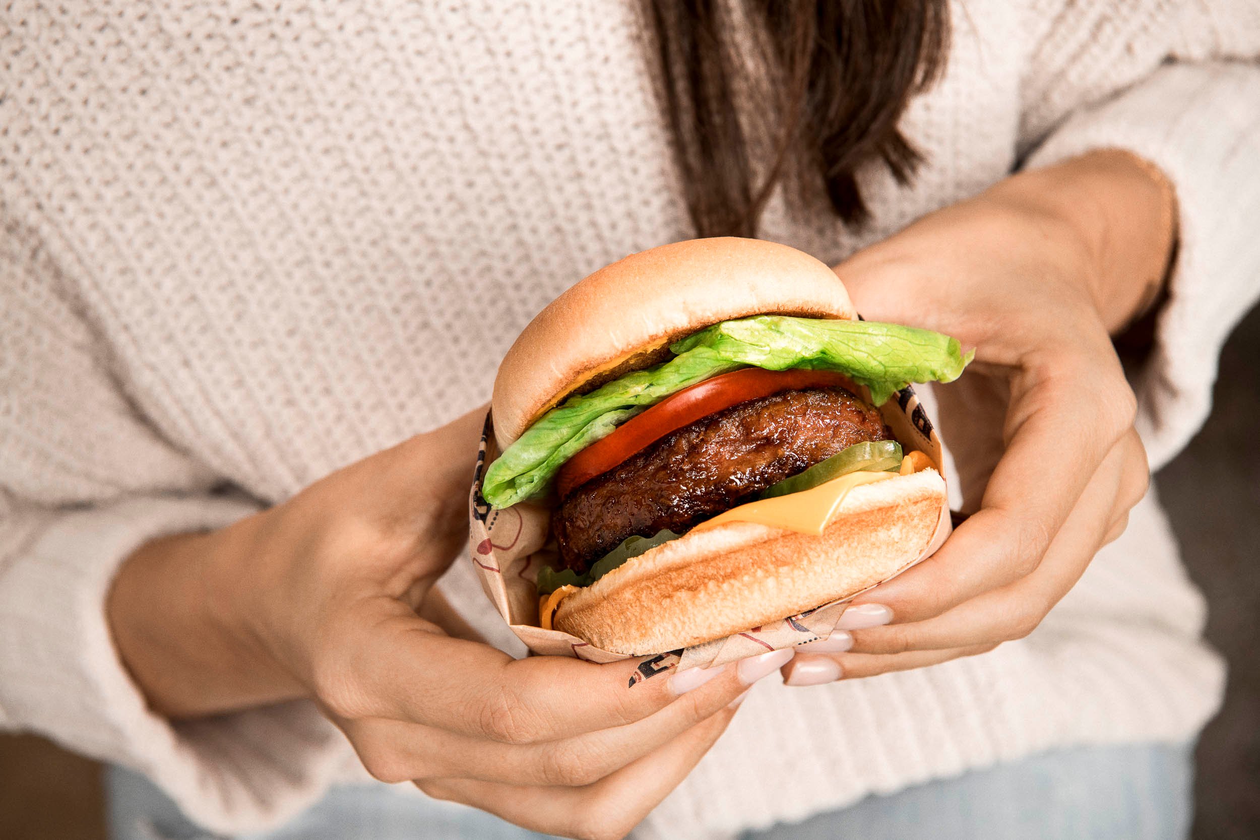 A woman holds a Beyond Meat burger with all the fixings.