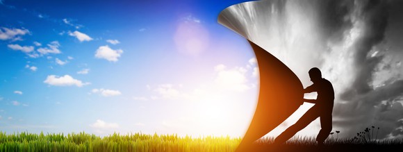 man pulling back the curtains from a dark world to a world with blue sky and green grass and sunshine