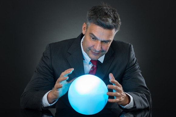 Man in a suit staring at a crystal ball that is hovering between his hands. 