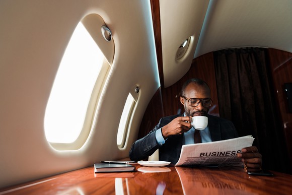 Man sitting near plane window reading newspaper and drinking coffee