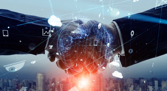 Two hands shaking with a globe superimposed on the  two hands. 