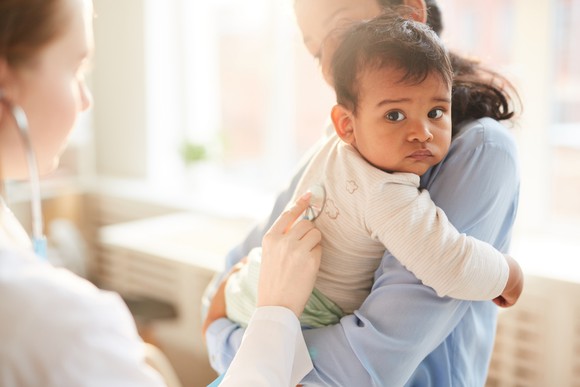 A doctor examines a baby being held in its mother's arms.