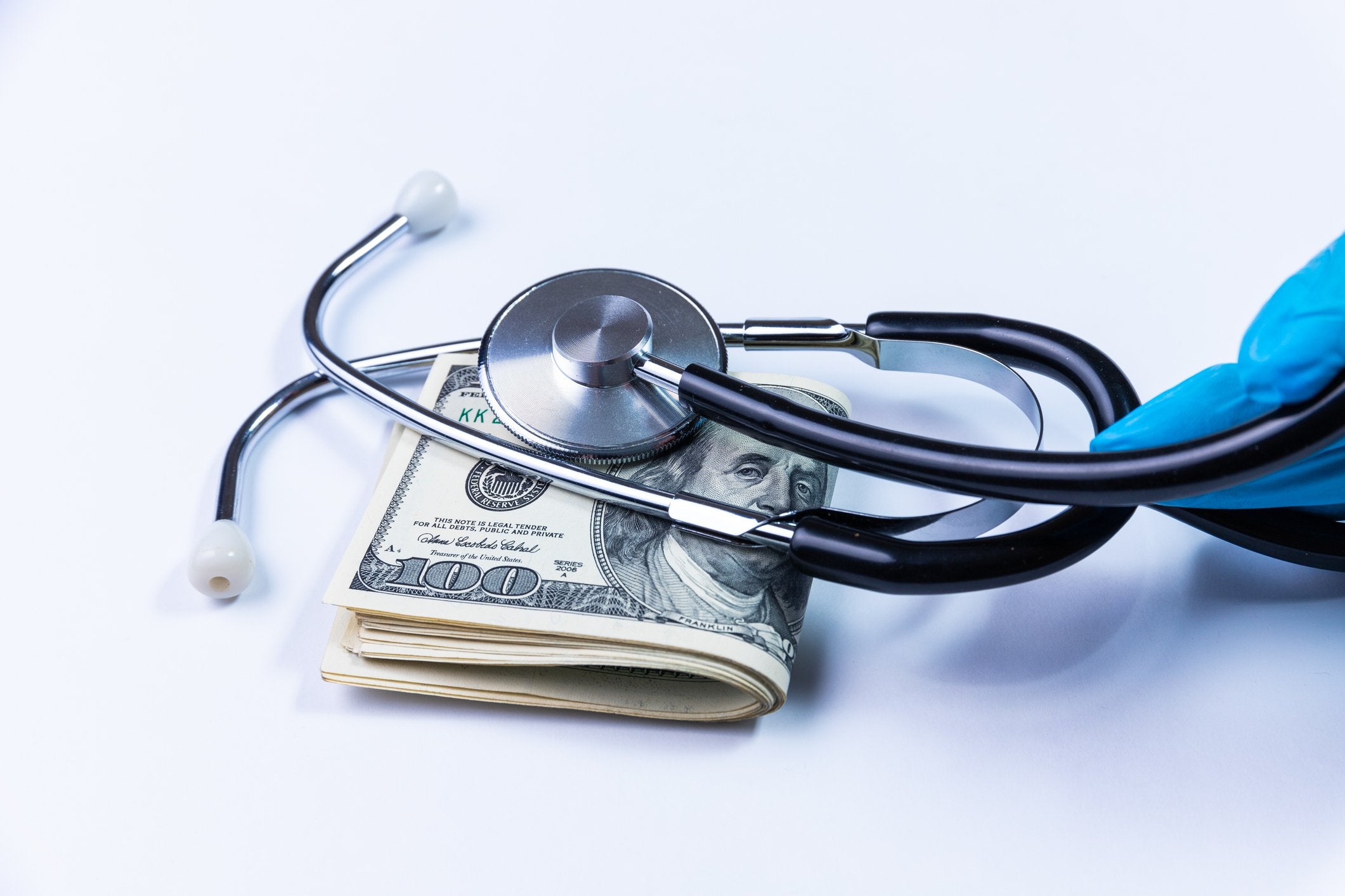 A stethoscope laying atop a pile of folded hundred dollar bills.