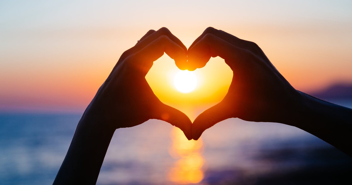 Two hands forming heart, with sun shining through.