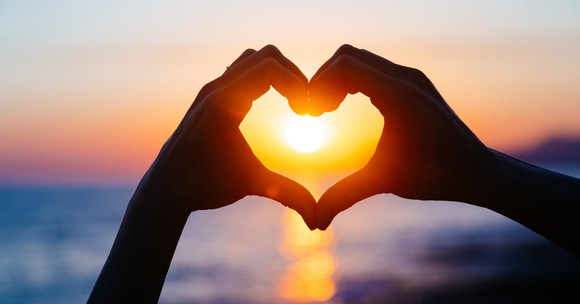 Two hands forming heart, with sun shining through.