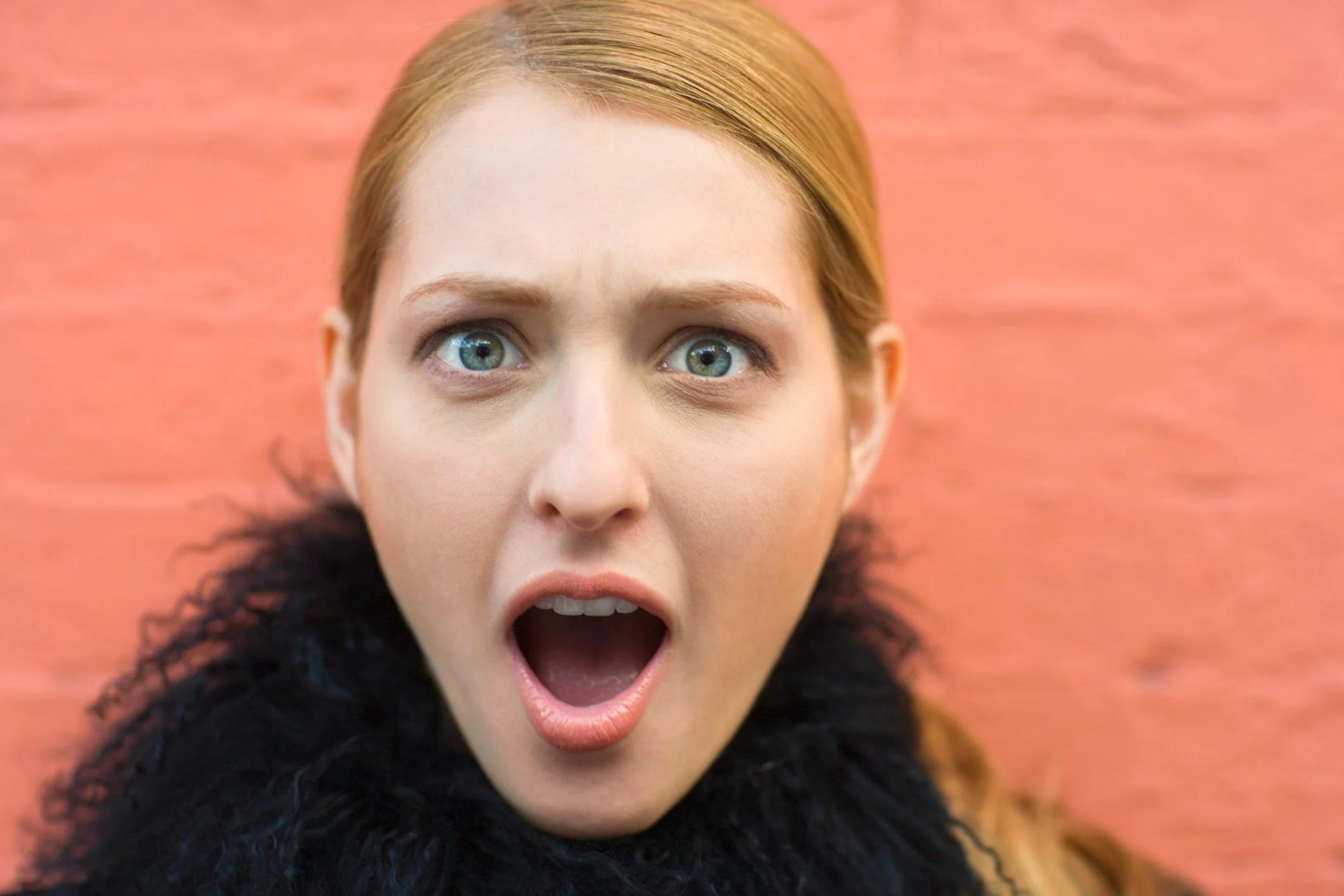 Person with surprised expression, against a flamingo-pink wall.