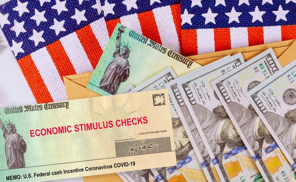 An economic stimulus check and hundred dollar bills on top of American flags.