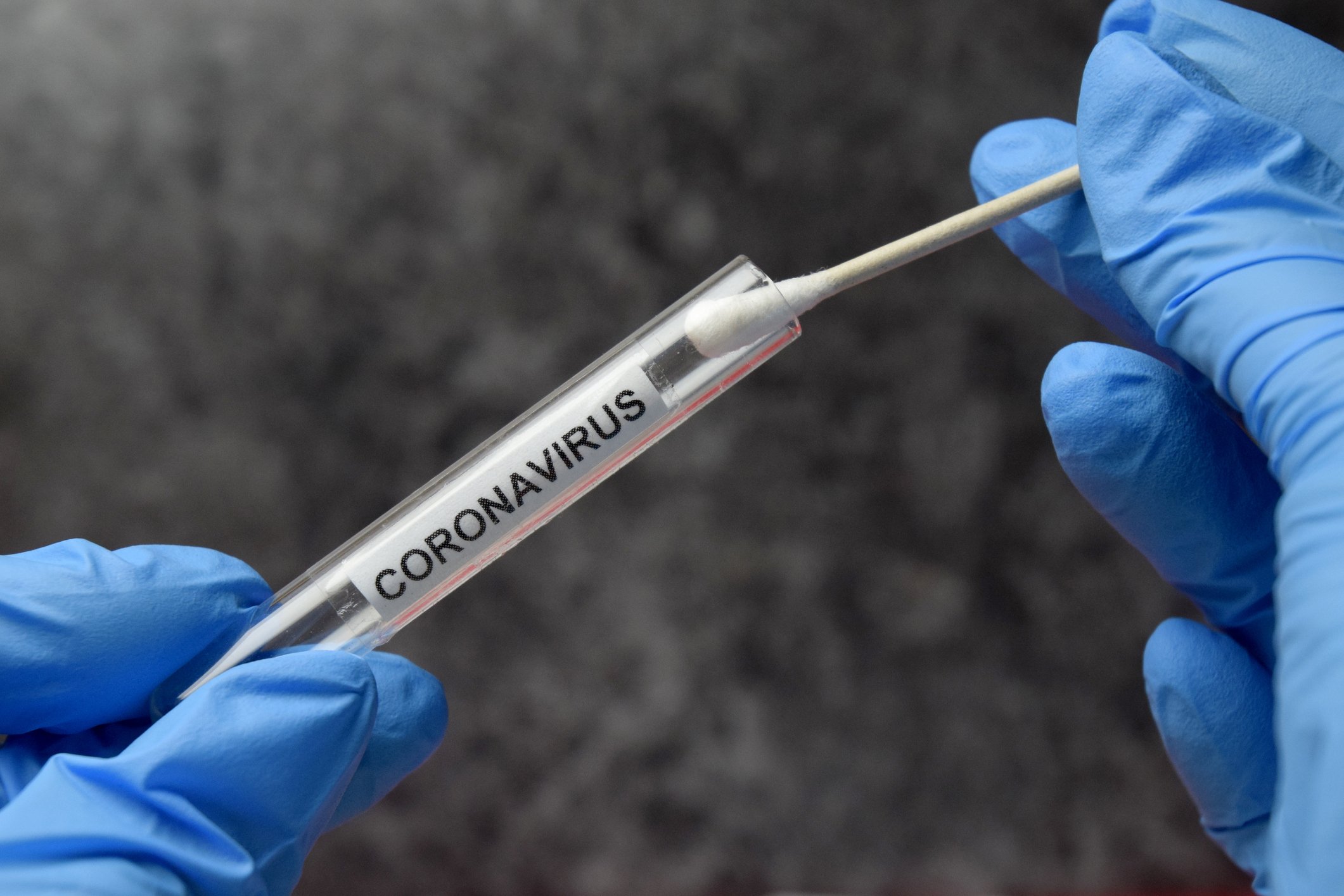 Medical professional placing a swab into a vial labeled "coronavirus." 