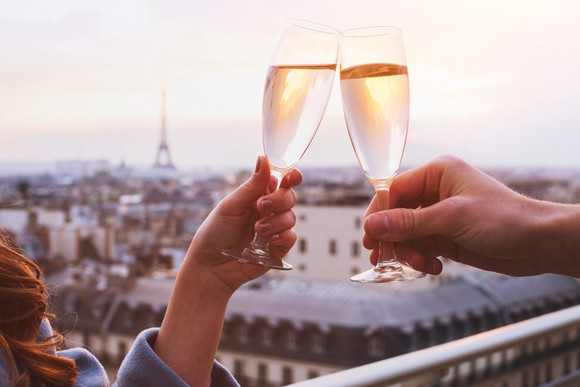 Two people clink  champagne glasses with a view of Paris in the background. 