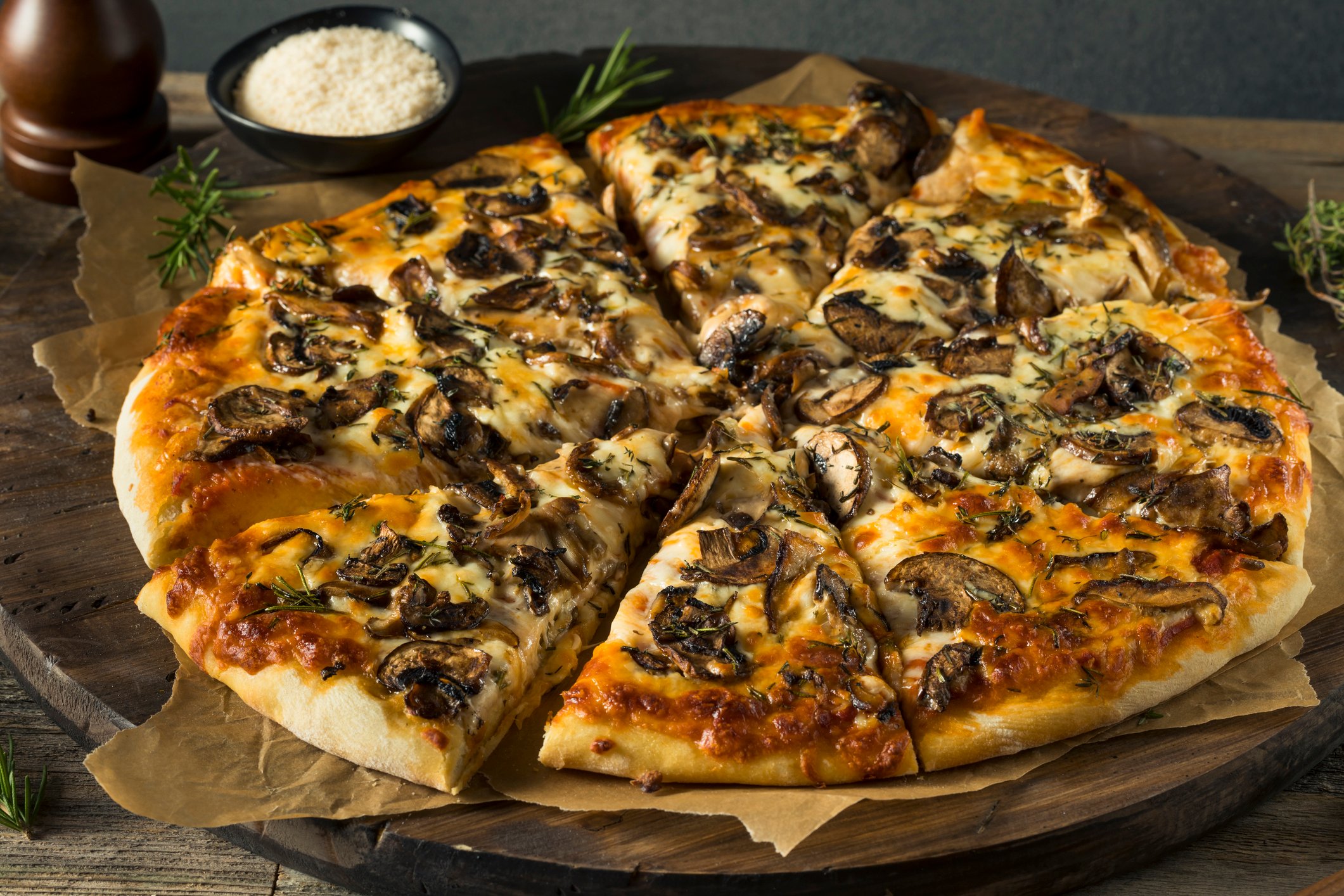 Mushroom pizza cut into eight slices, with a saucer of grated cheese beside it.