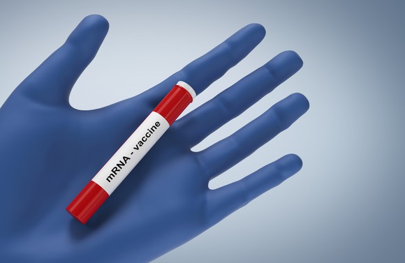 mRNA vaccine printed on the label of a vial held in a gloved hand. 
