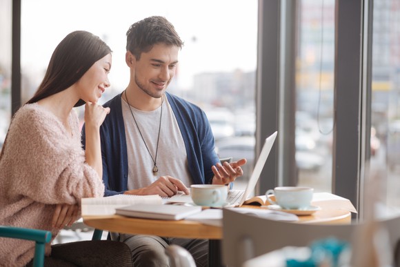 Young couple at a table looking at a laptop screen. 