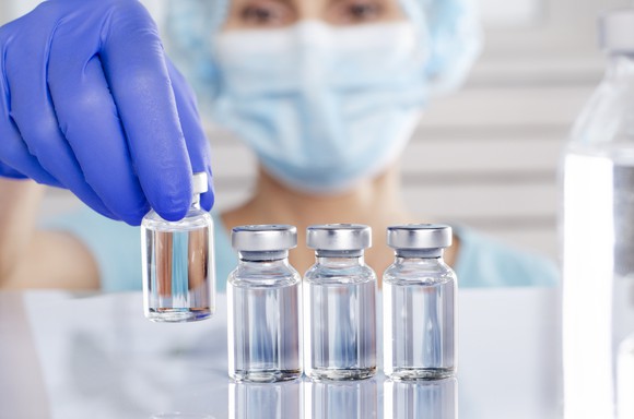 Masked technician with vials of medicine.