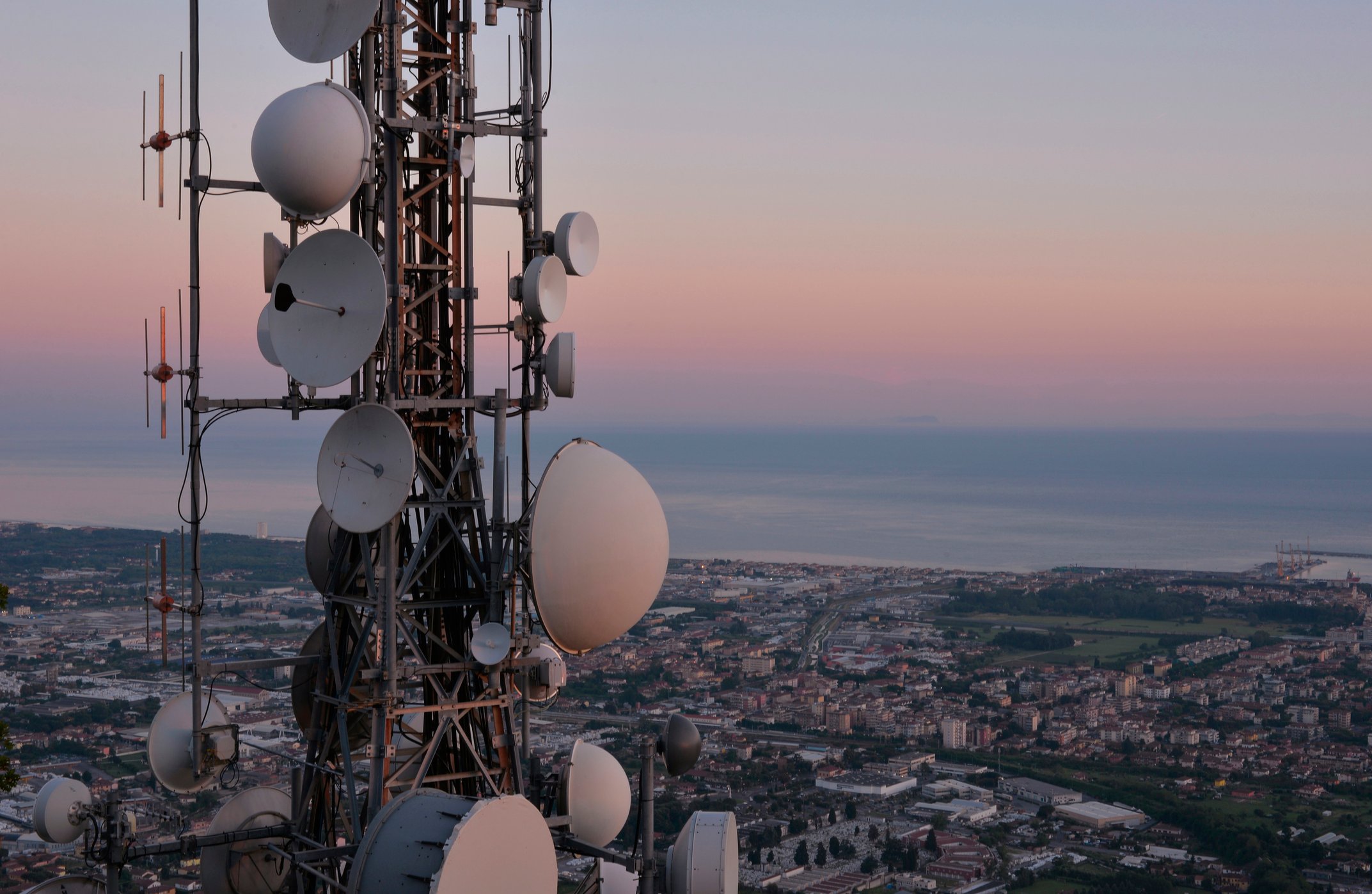 A tower laden with large radios looking over a seaside town. 
