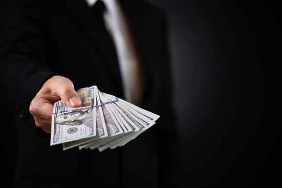 Someone in suit with handful of hundred dollar bills