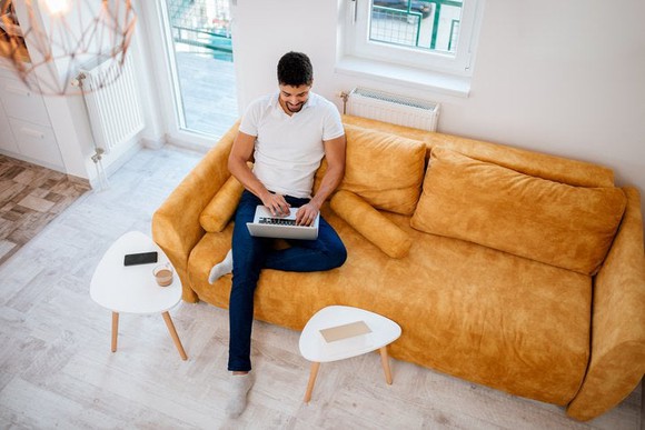 Aeriel view of a man using a laptop while sitting on his couch.