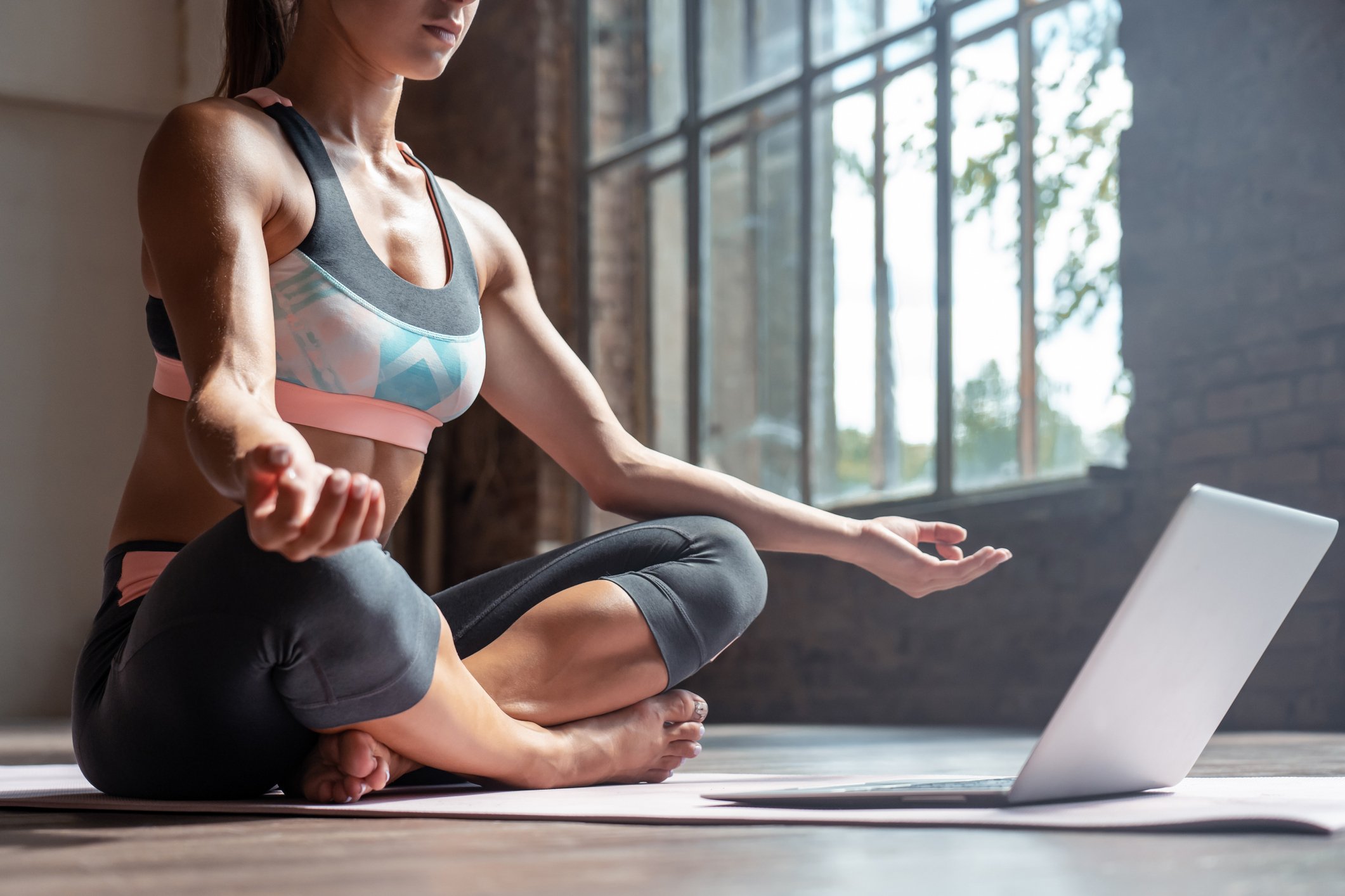 A woman meditating on the floor with a laptop.