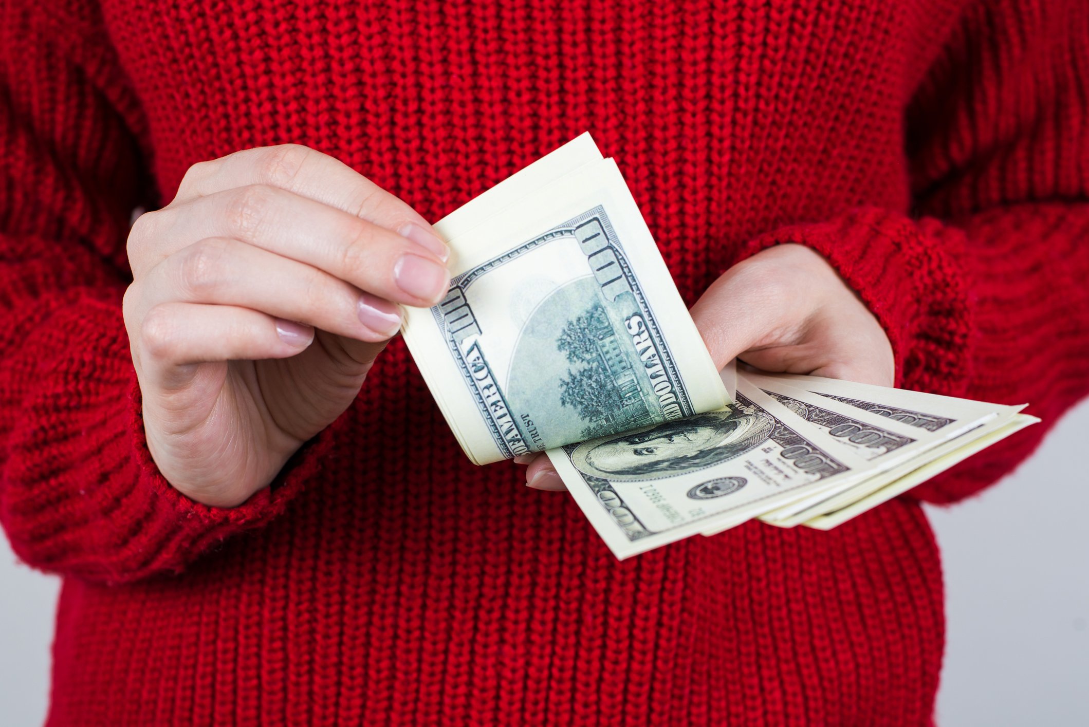 A woman's hands hold out a handful of hundred dollar bills.