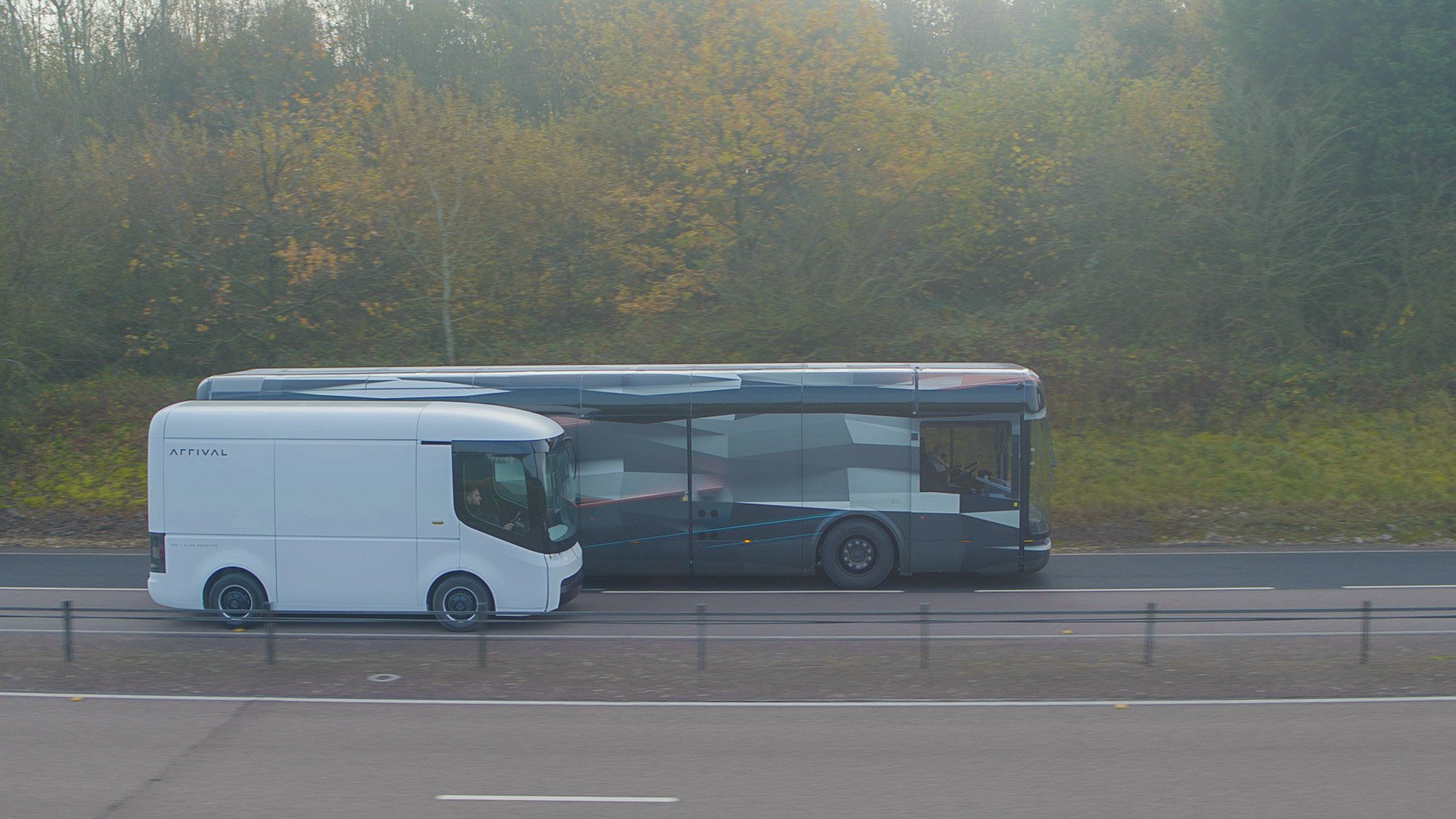 Arrival electric bus and van travel next to each other on a road.