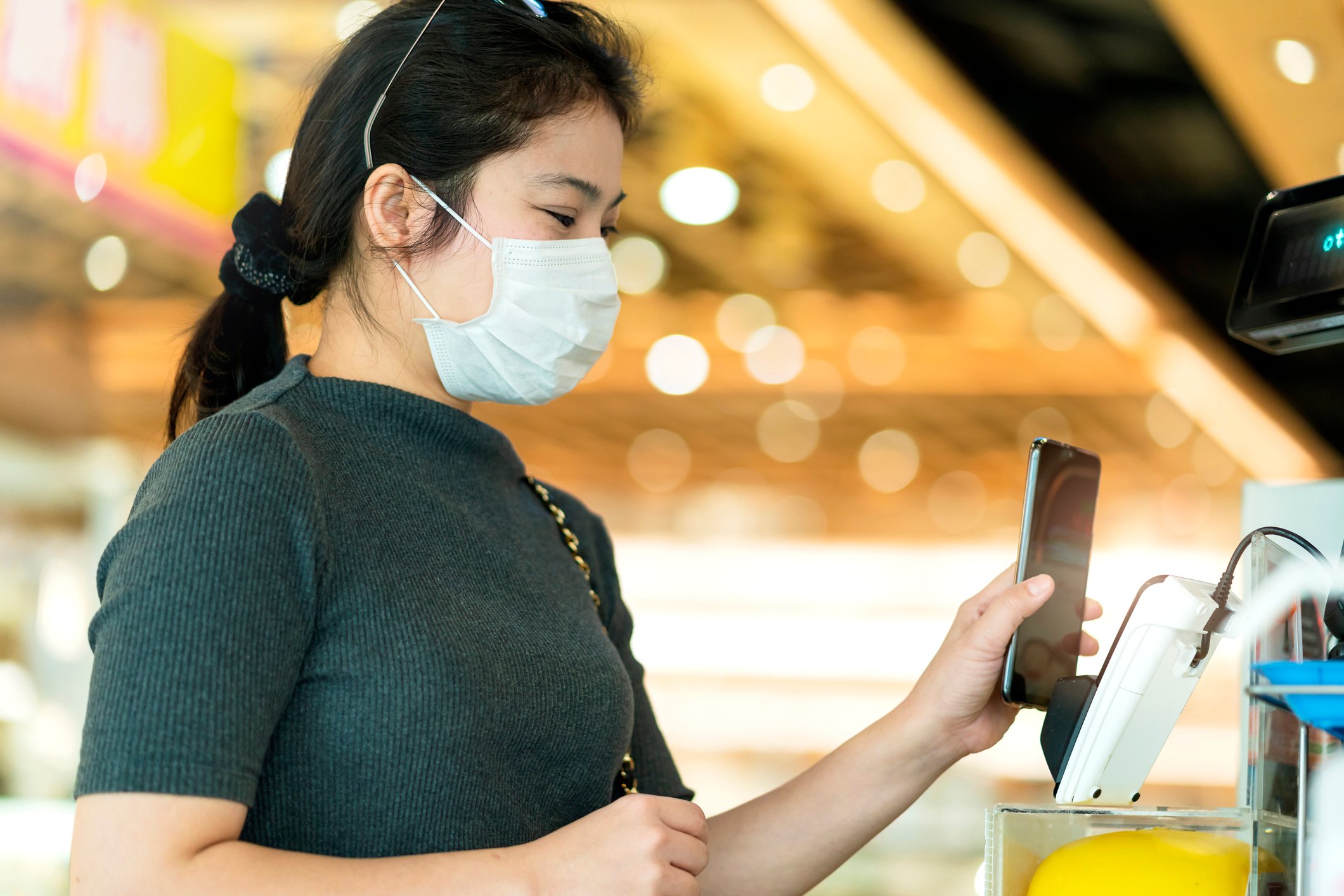 A woman wearing a mask paying for concessions with her phone. 