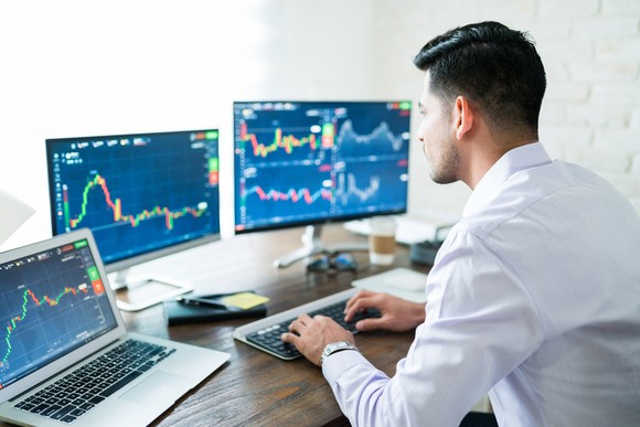 Man looking at stock charts on three computer screens