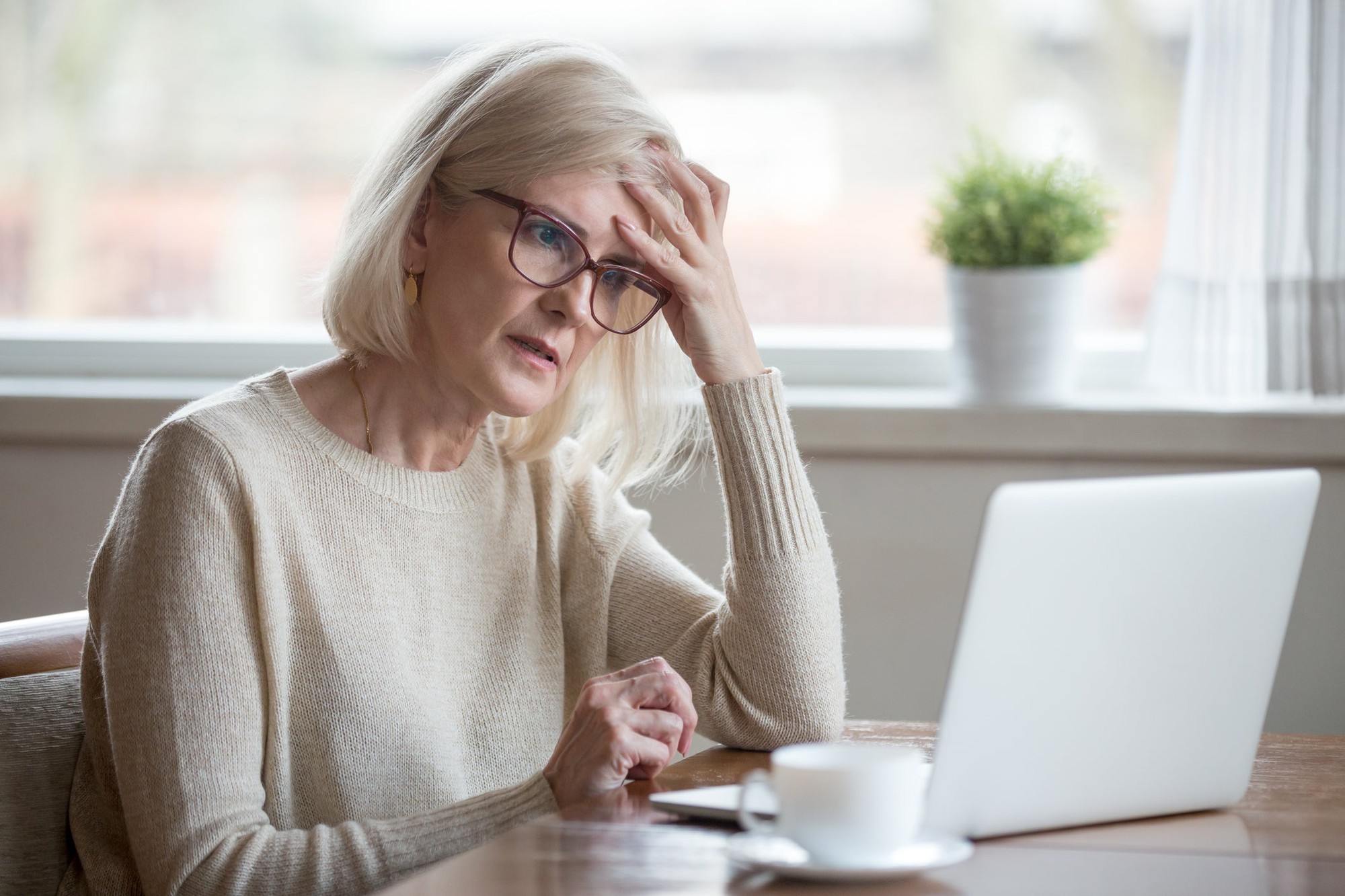 A woman with a hand to her forehead as she eyes her open laptop.