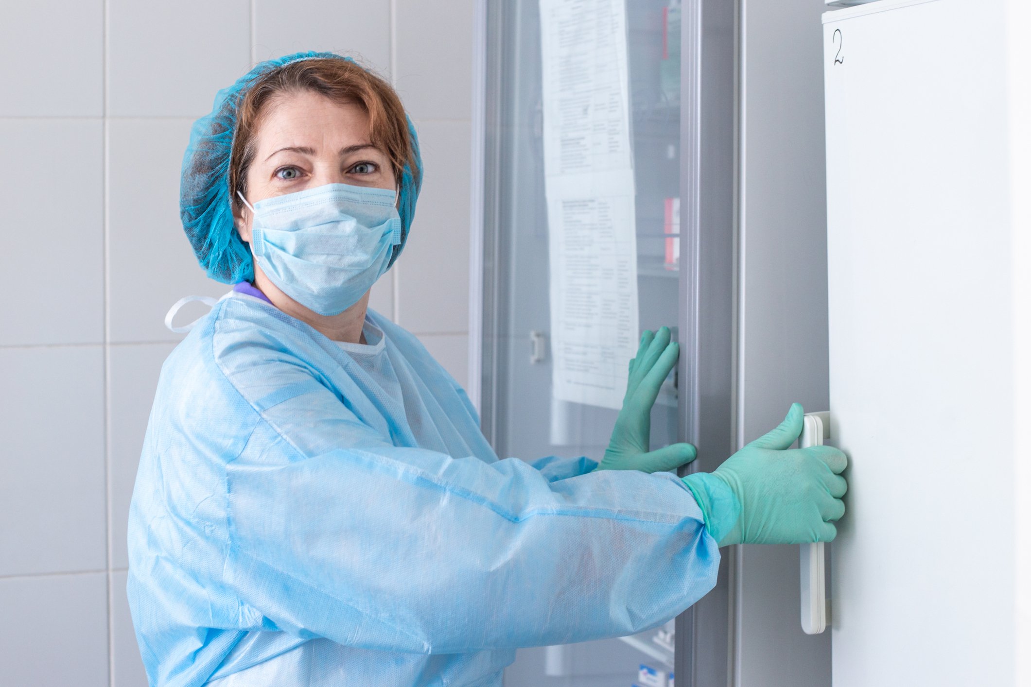 Woman in protective equipment opening a large medical refrigerator