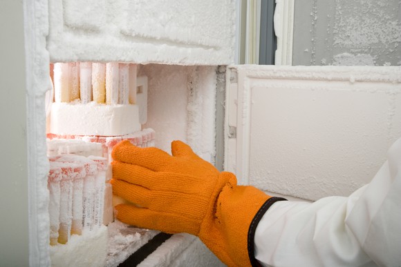 A gloved and suited person reaching into a deep freezer for vaccines.