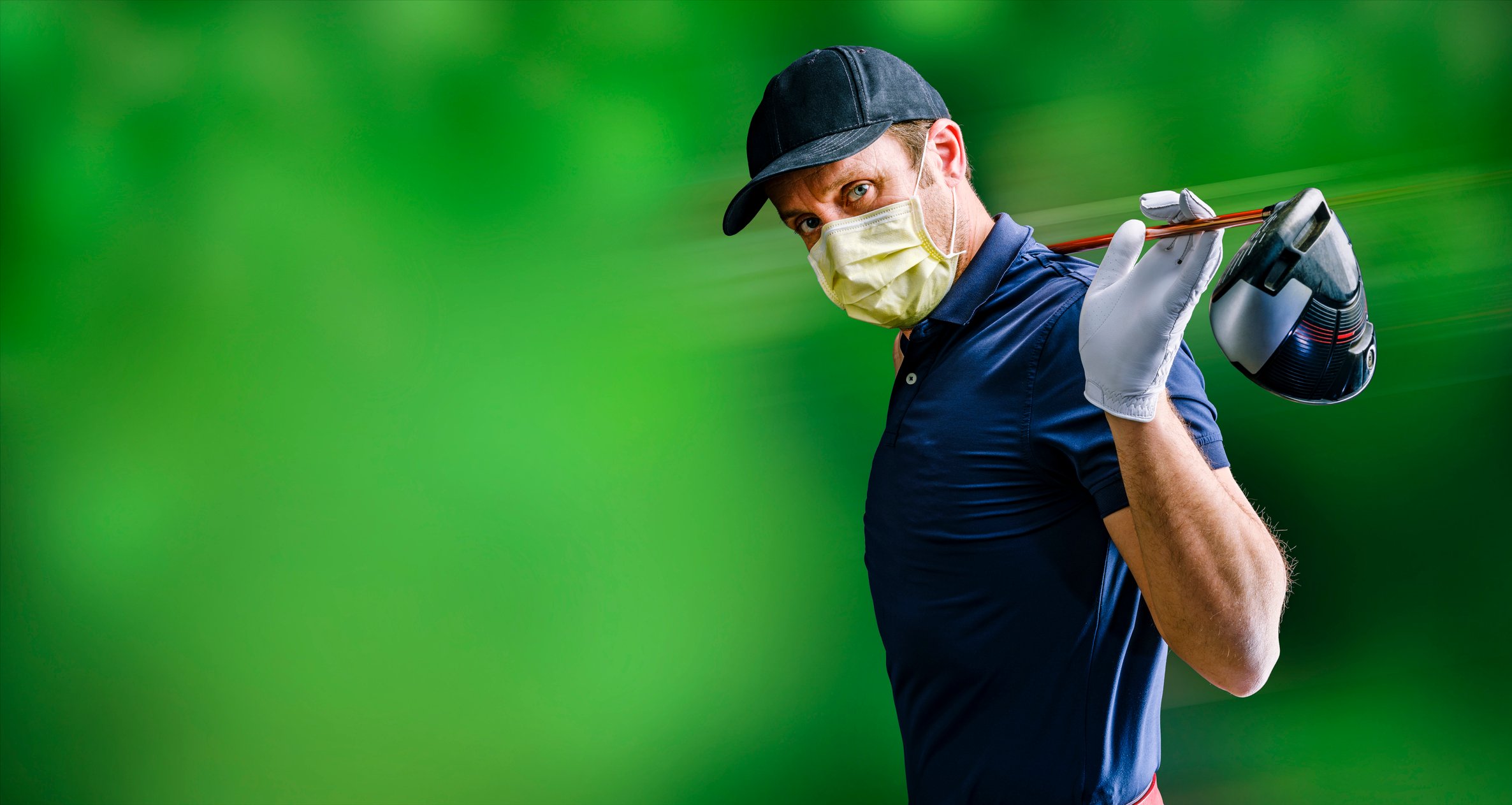 A male golfer  stretches with his driver  behind his head and wears a face mask. 