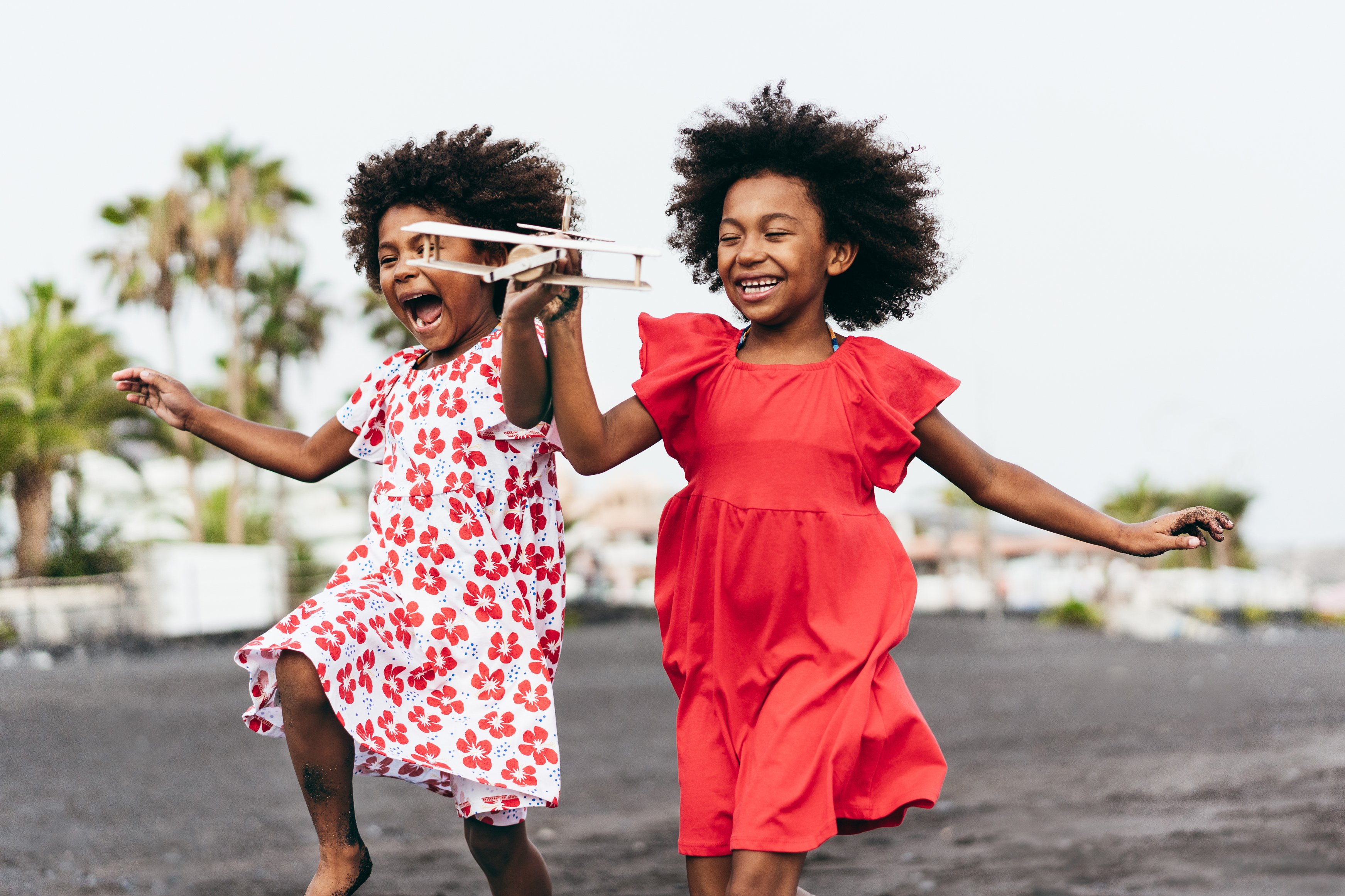 Twin African girls run with glee while holding a wooden airplane.