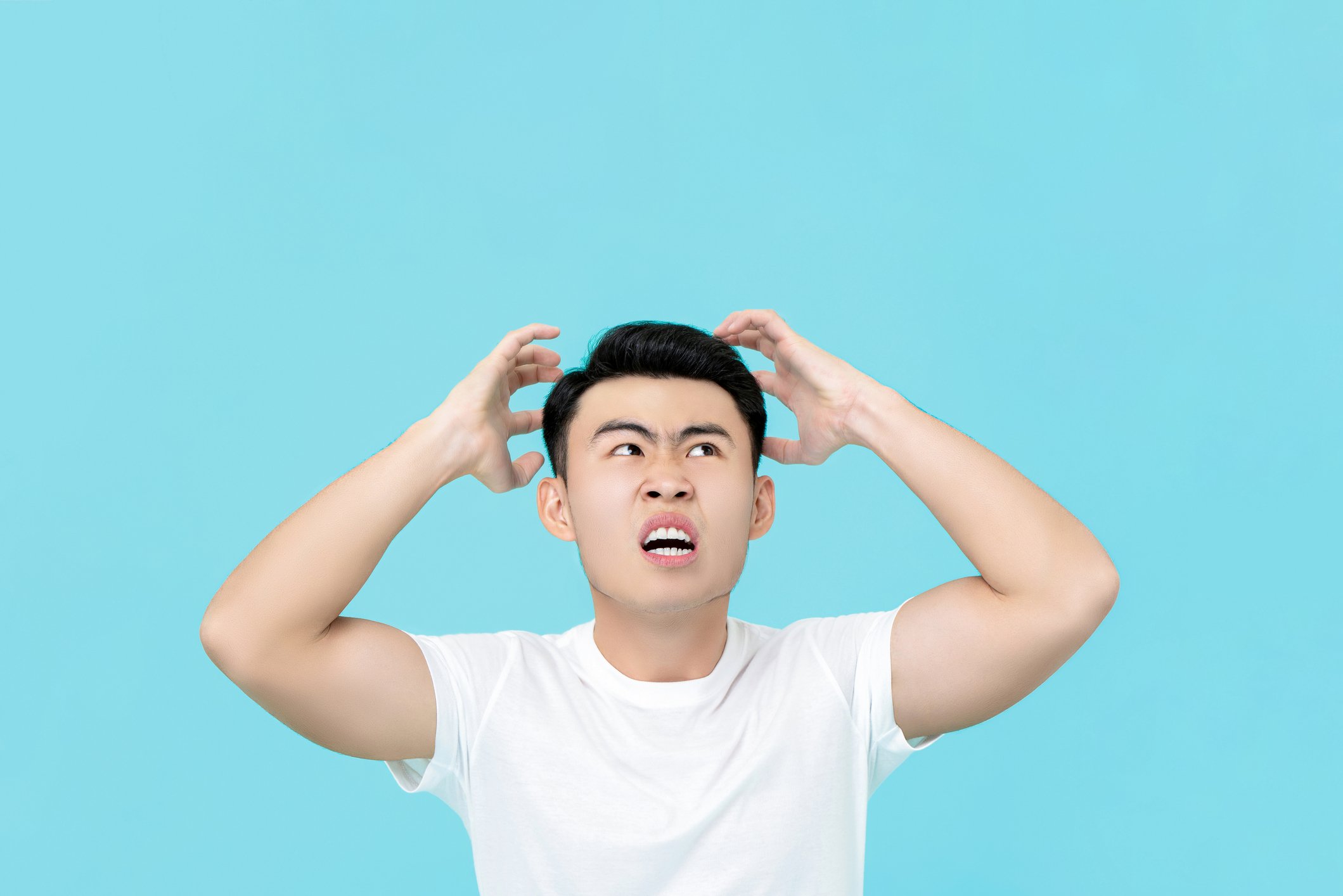 A young man cringes at something against a light blue background. 